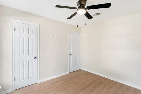 an empty room with wooden floor closet and fan