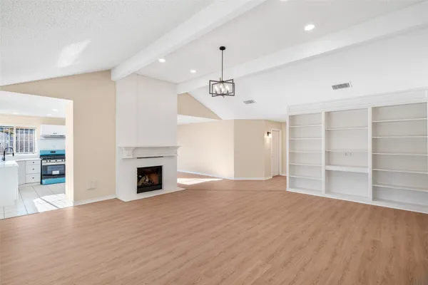 a view of an empty room with wooden floor fireplace and a window