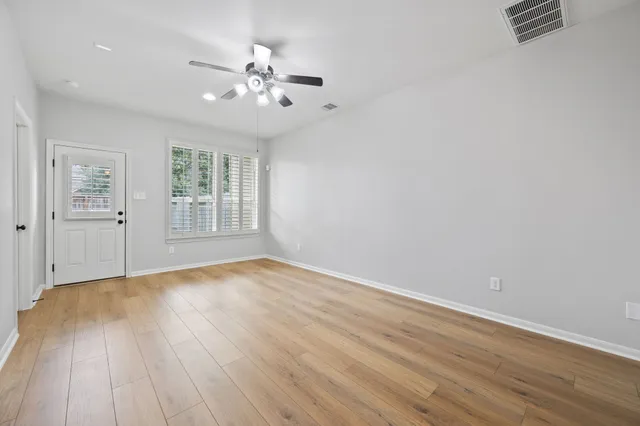 an empty room with wooden floor chandelier fan and windows