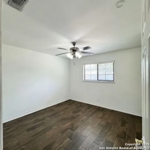 an empty room with wooden floor fan and windows
