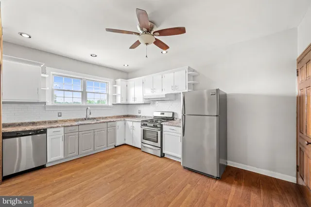 a kitchen with stainless steel appliances granite countertop a refrigerator a sink dishwasher a stove with white cabinets and wooden floor