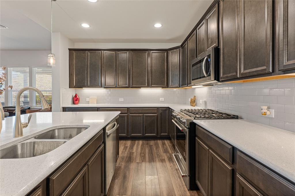 9517 Sunset Lane Oak Point, TX 75068 - Photo 16 of 40 9517 Sunset Lane, Oak Point, TX 75068 - kitchen - Kitchen with stainless steel appliances, dark wood finish cabinets, dark wood finished floors, decorative light fixtures, and light stone countertops