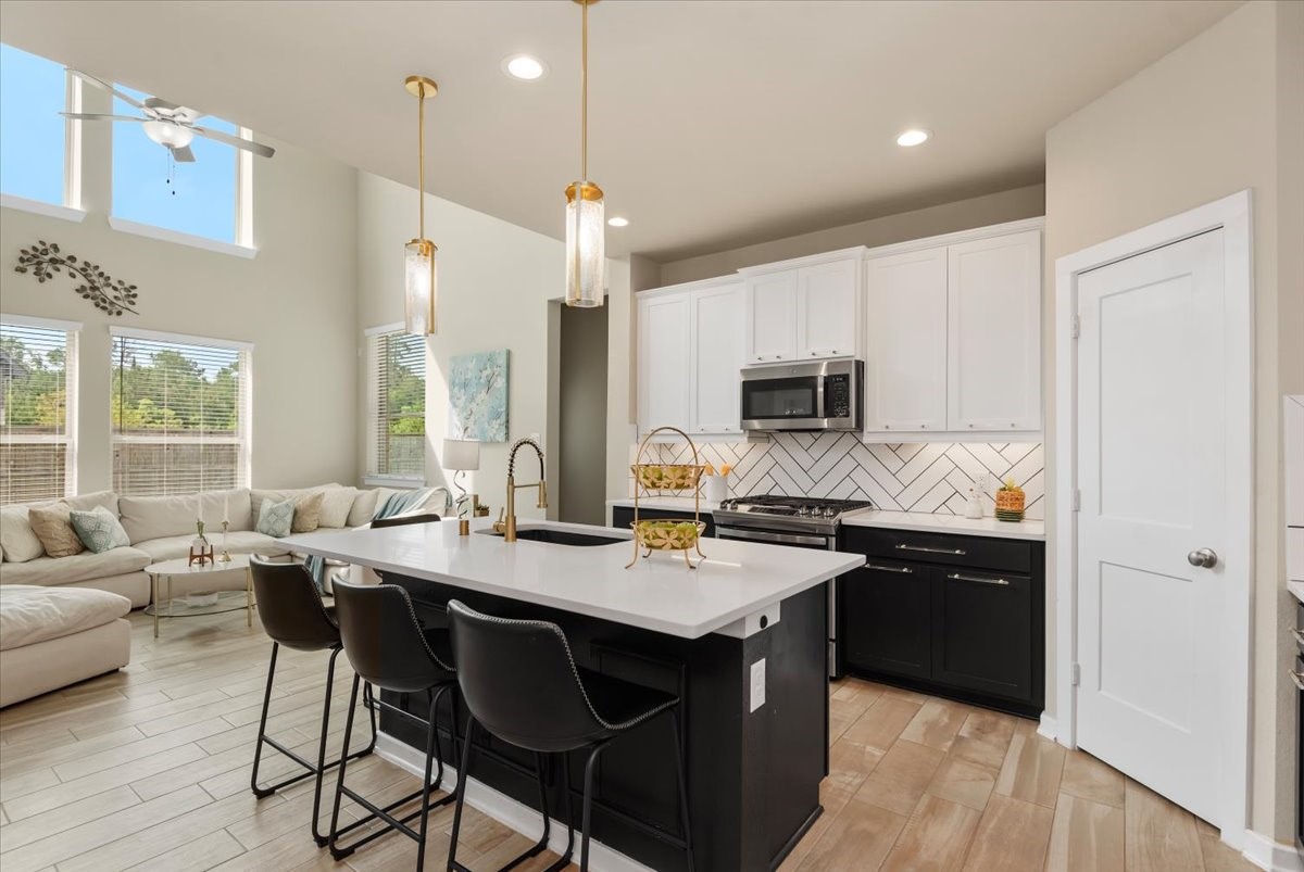 17814 Tree Of Heaven Conroe, TX 77385 - Photo 3 of 48 Modern open-concept kitchen featuring a large quartz island with seating, sleek cabinetry, and stylish backsplash, seamlessly flowing into the bright living area with soaring ceilings and abundant natural light—perfect for everyday living and entertaining.