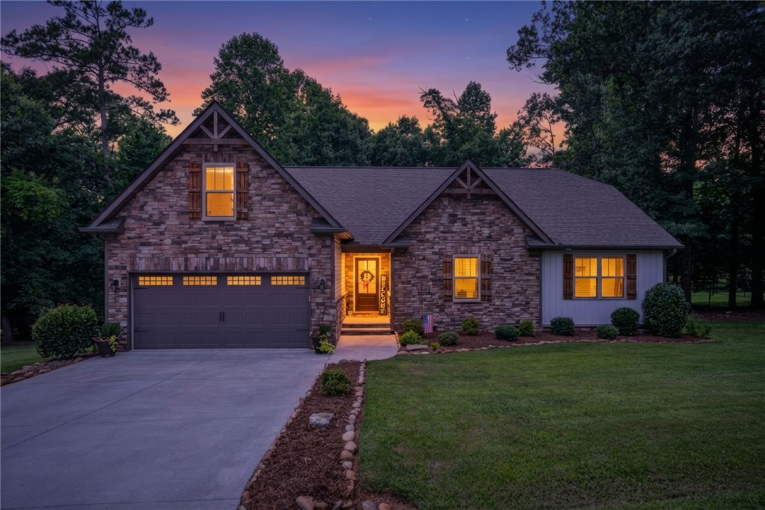 201 Hearthstone Drive Anderson, SC 29621 - Photo 1 of 49 A stone and siding facade home with illuminated windows, surrounded by mature trees at twilight.