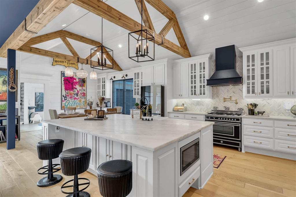 1901 Spring Mountain Road Cross Roads, TX 76227 - Photo 16 of 40 Vaulted ceiling with exposed wood beams, white cabinetry with glass-front uppers, a large kitchen island with integrated microwave, a black range with coordinating hood, and light wood-finish flooring