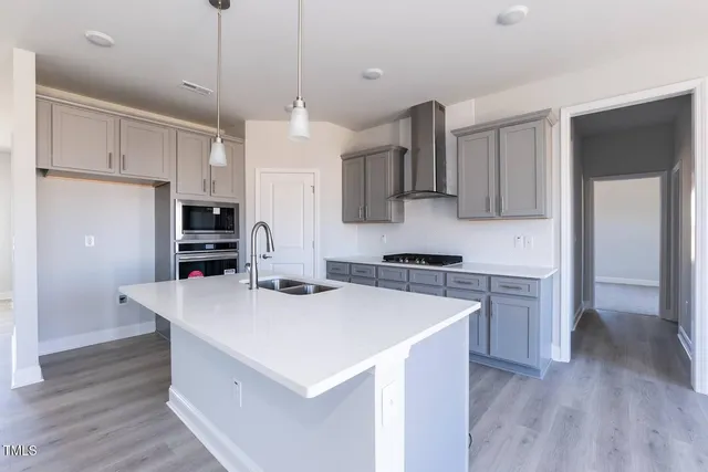 a kitchen with stainless steel appliances a stove a sink a refrigerator and white cabinets with wooden floor