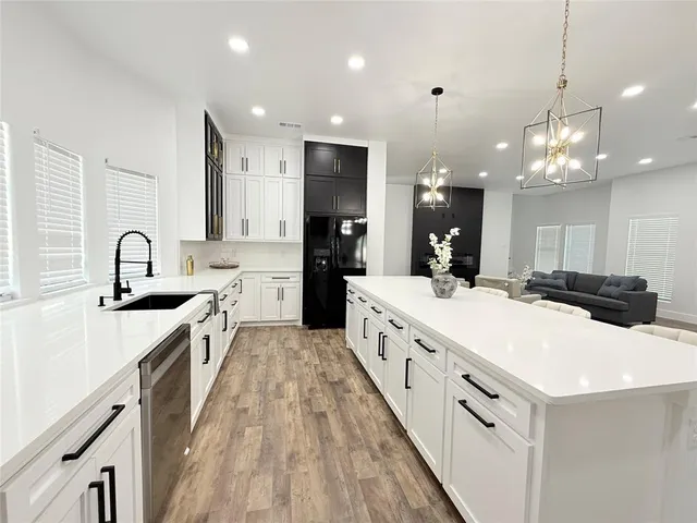 a large white kitchen with a large island oven a sink dishwasher and white cabinets with wooden floor