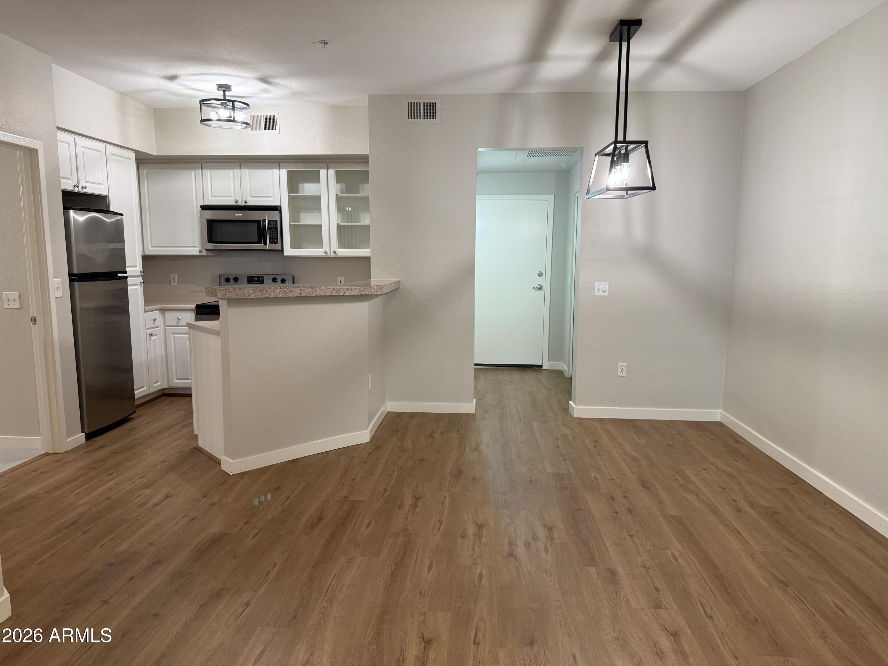 a view of empty room with wooden floor and kitchen