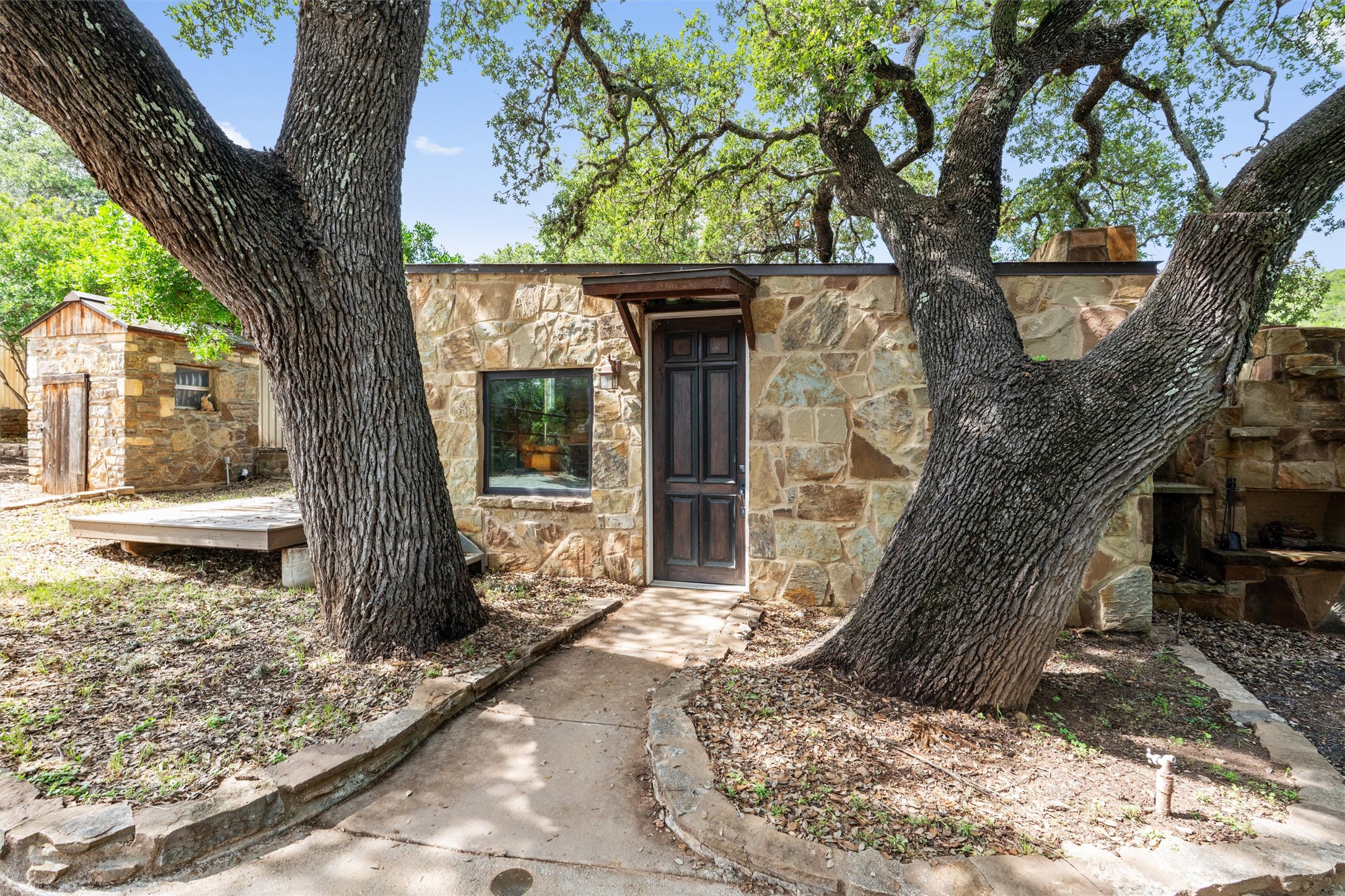 325 Eagle Rest Burnet, TX 78611 - Photo 18 of 40 Mature trees flank a stone-clad cabin with a dark wood door, offering a private, rustic appeal.