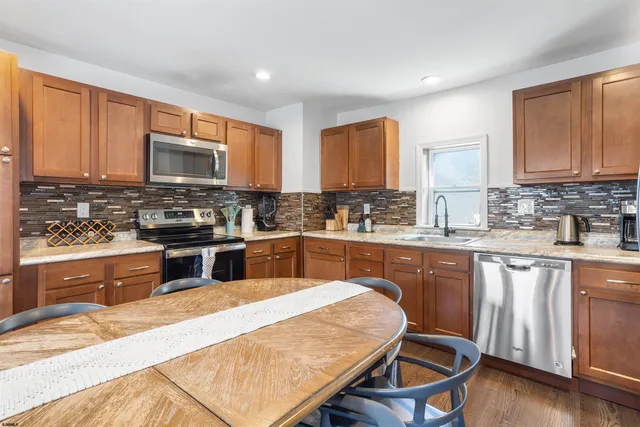 a kitchen with stainless steel appliances granite countertop a stove top oven a sink dishwasher a dining table and chairs with wooden cabinets