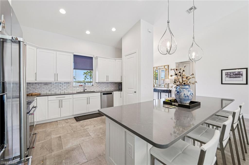 161 Tahiti Circle Naples, FL 34113 - Photo 10 of 42 Kitchen with a breakfast bar, white cabinets, stainless steel appliances, a center island, and hanging light fixtures