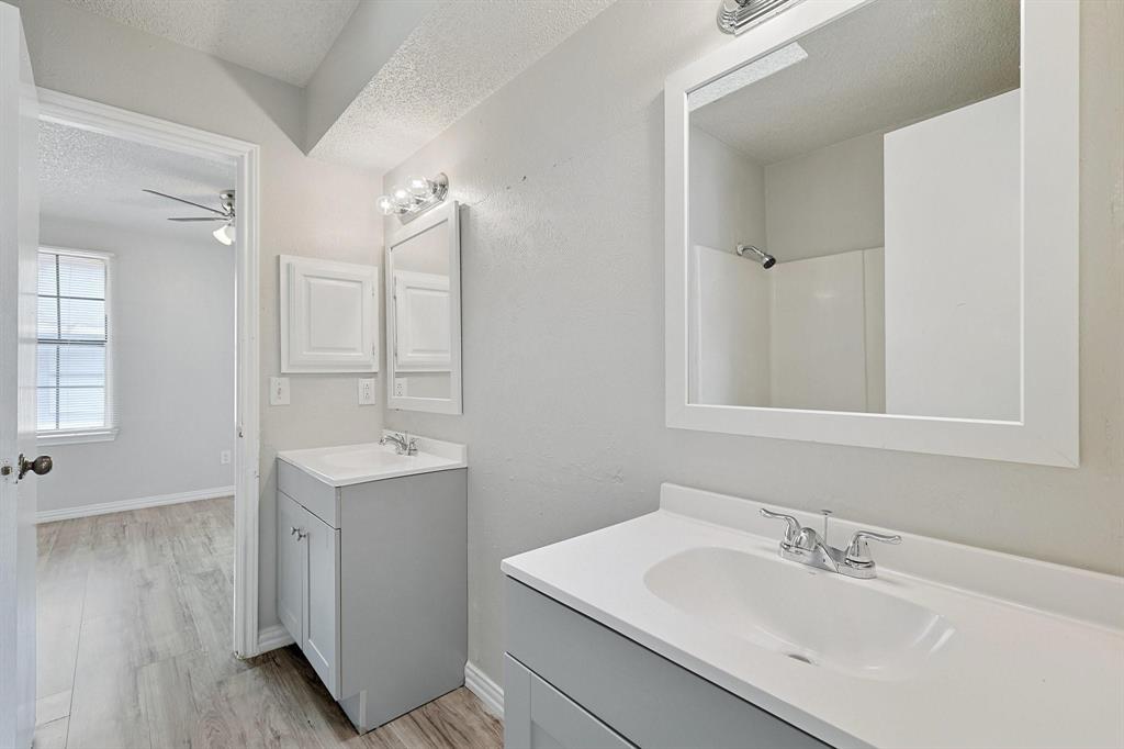 Bathroom featuring a textured ceiling, two vanities, light wood-style floors, and ceiling fan