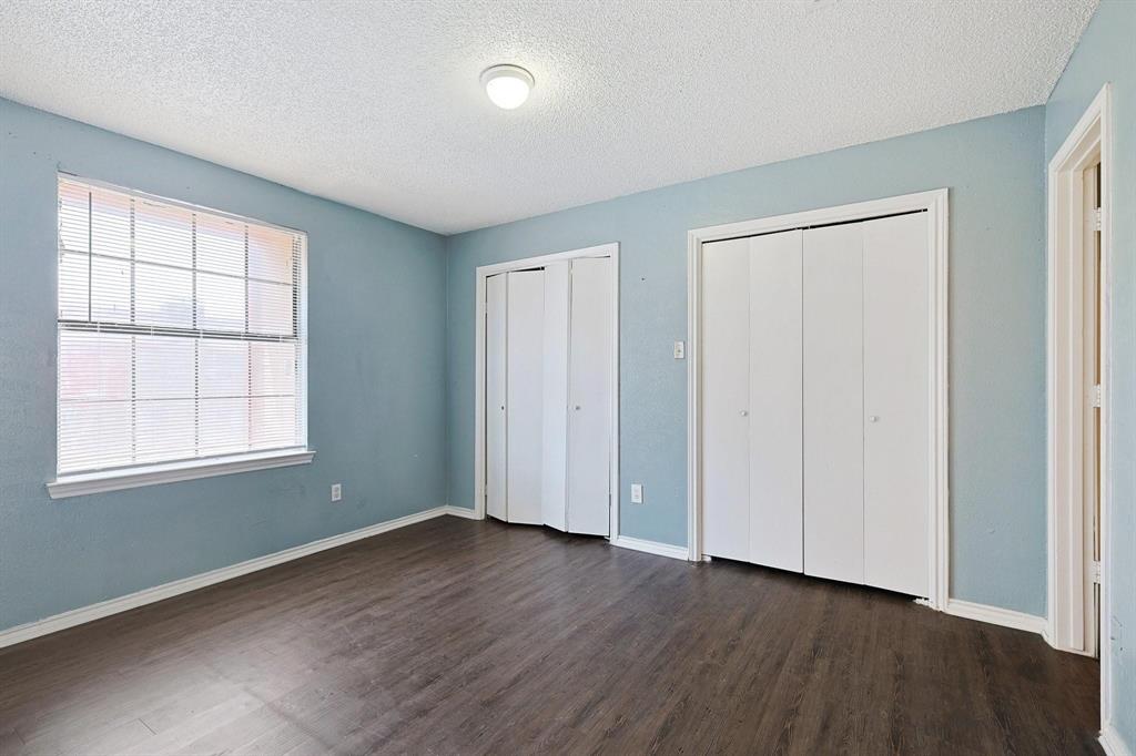 8005 Rothington Road, Unit 1117 Dallas, TX 75227 - Photo 6 of 13 Unfurnished bedroom with a textured ceiling, two closets, and dark wood-style flooring