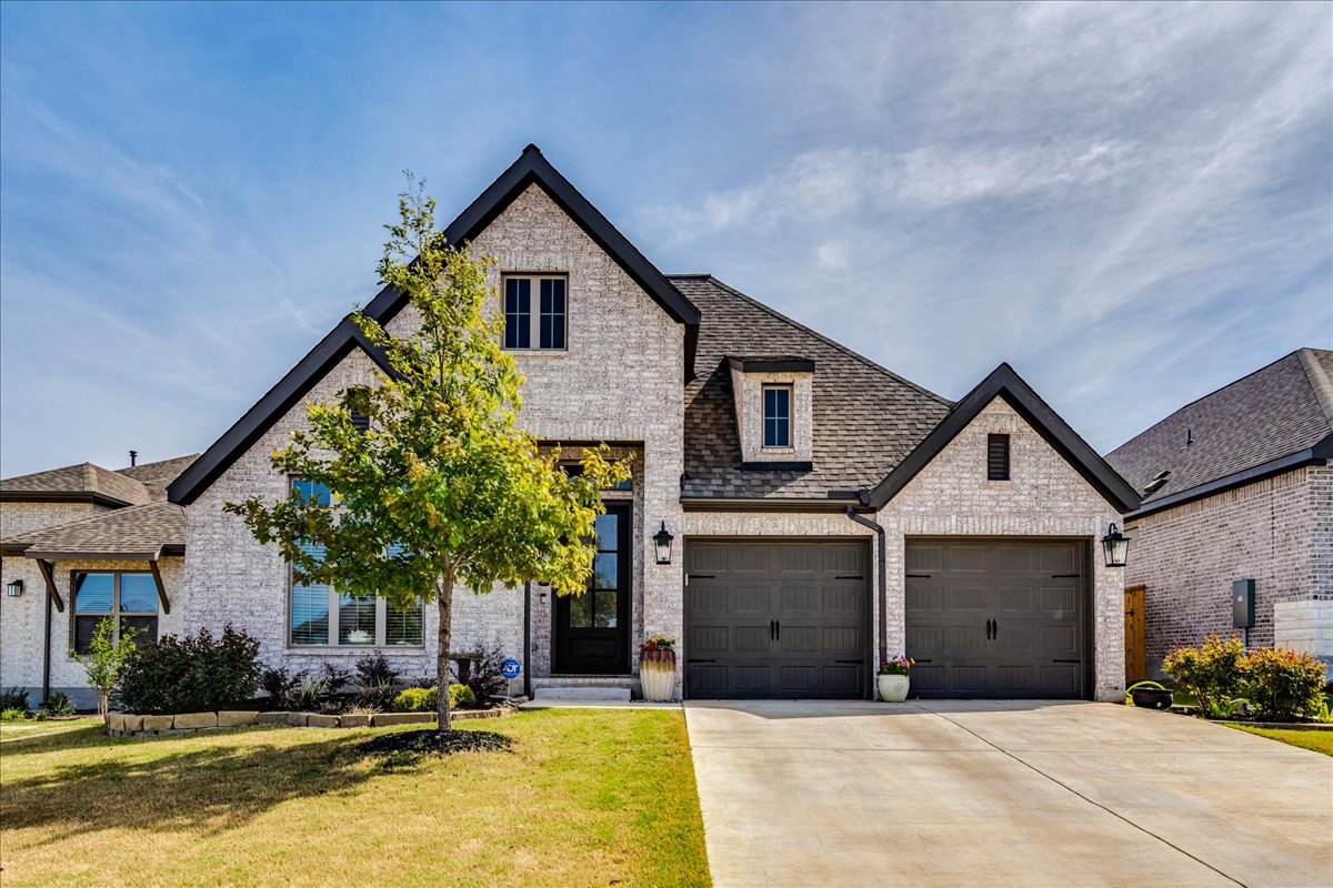 French country style house featuring concrete driveway, brick siding, a front lawn, a shingled roof, and an attached garage