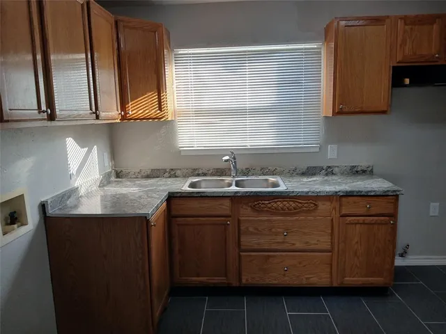 a sink with granite countertop cabinets and window