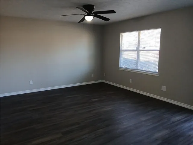 an empty room with wooden floor fan and windows