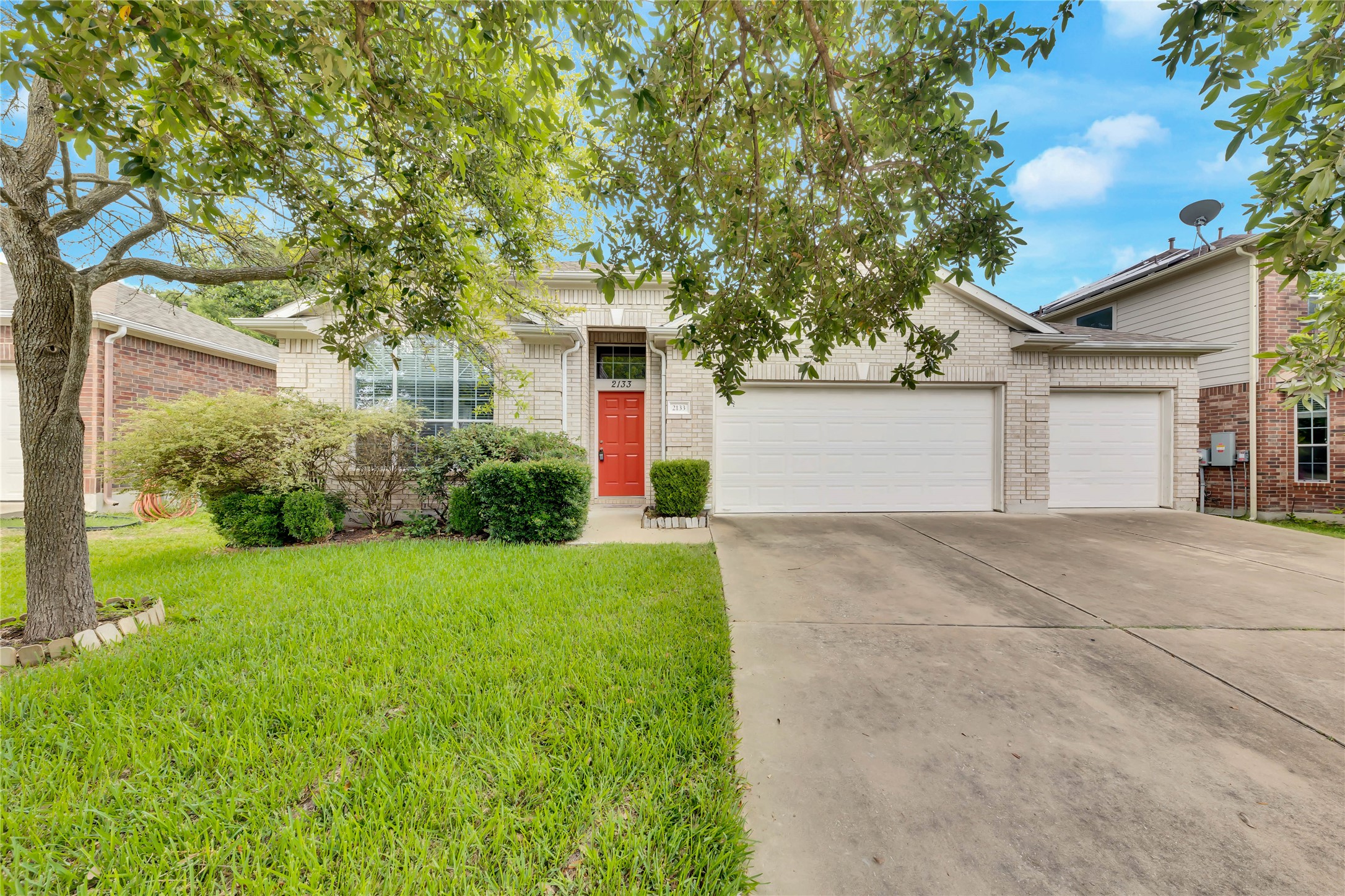 2133 Paradise Ridge Drive Round Rock, TX 78665 - Photo 2 of 22 Stone facade exterior with an orange entry door, mature landscaping, and a three-car garage