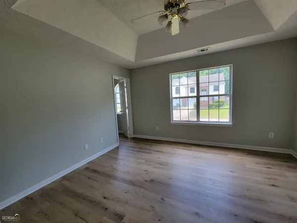 an empty room with wooden floor chandelier fan and windows