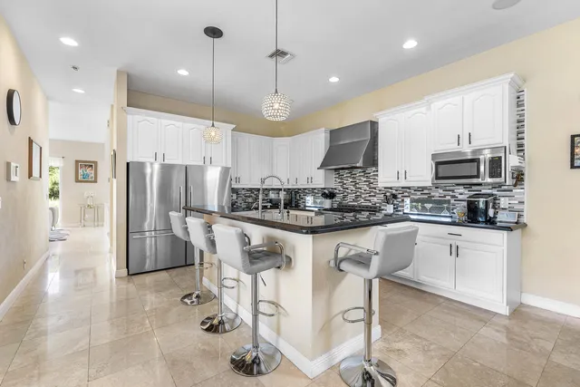 a kitchen with stainless steel appliances kitchen island granite countertop a refrigerator a stove a sink a microwave and white cabinets with wooden floor