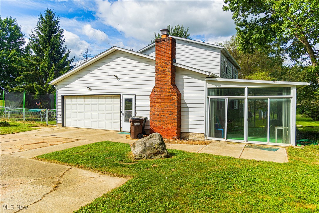 16974 Hawley Road Oberlin, OH 44074 - Photo 33 of 42 Back of house with a sunroom, driveway, a yard, an attached garage, and a chimney