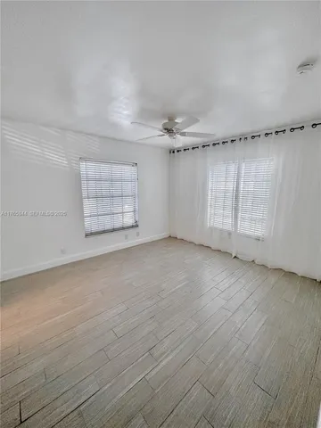 an empty room with wooden floor fan and windows
