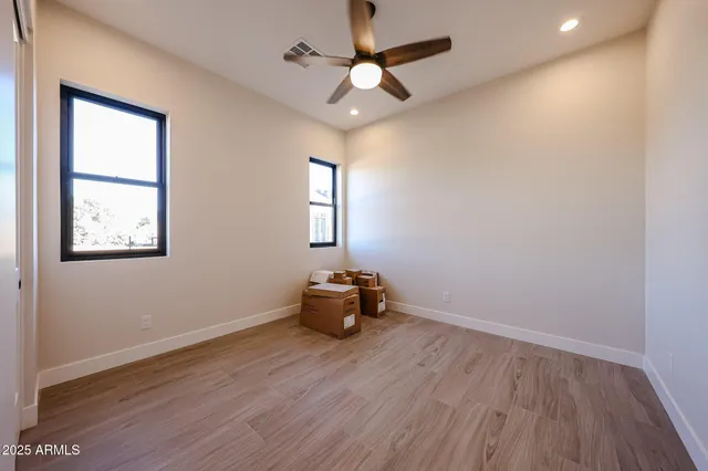 an empty room with wooden floor chandelier fan and windows