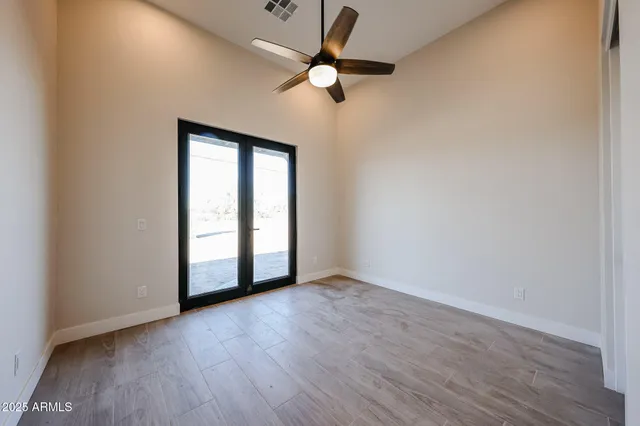 an empty room with wooden floor chandelier fan and windows