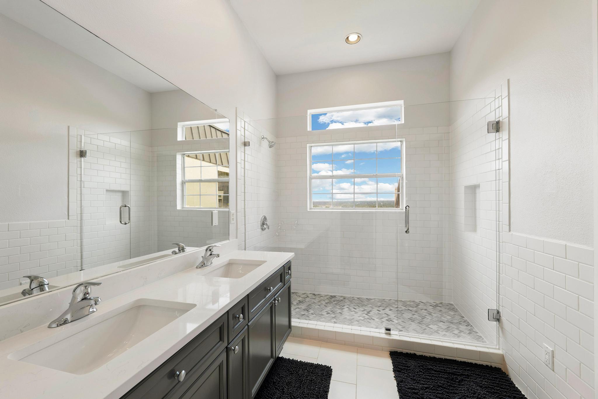 2918 Ranch Road 620, Unit J162 Austin, TX 78734 - Photo 21 of 26 Contemporary primary bathroom with dual vanity, white subway tile accents, and a spacious glass-enclosed shower with pebble-style flooring and built-in niches
