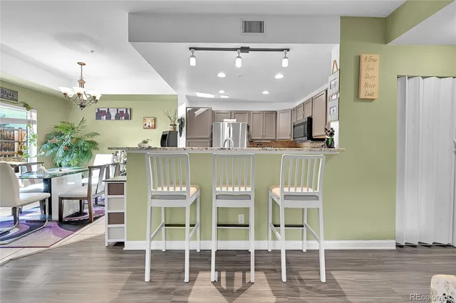a kitchen with stainless steel appliances kitchen island granite countertop a dining table chairs and a refrigerator
