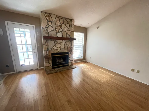 an empty room with wooden floor fireplace and windows