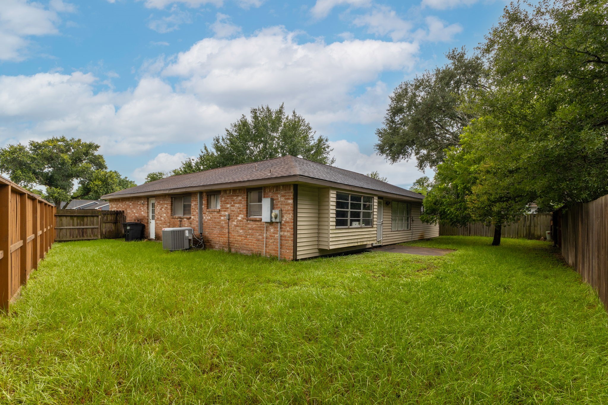 14110 Eventide Drive Cypress, TX 77429 - Photo 25 of 27 Backyard of the house with a spacious grassy area, wooden fencing, and mature trees providing shade. The house features a single-story design with a mix of brick and siding exterior.