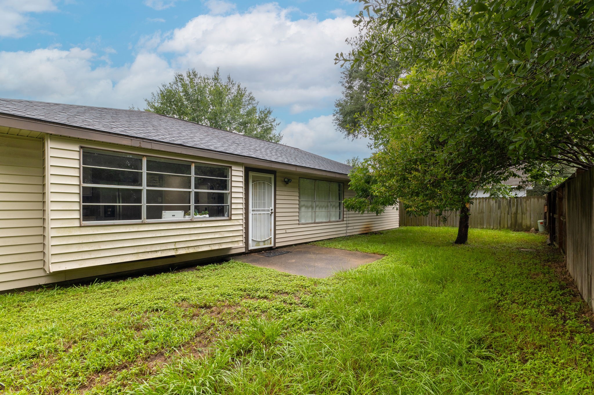 14110 Eventide Drive Cypress, TX 77429 - Photo 26 of 27 Backyard of the house with a spacious grassy area, wooden fencing, and mature trees providing shade. The house features a single-story design with a mix of brick and siding exterior.