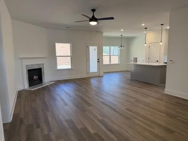 an empty room with wooden floor a ceiling fan and kitchen view