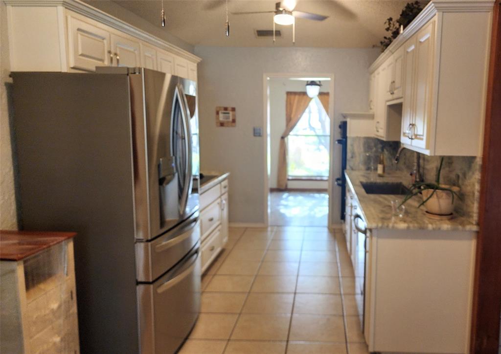 7505 Patsy Court Arlington, TX 76016 - Photo 13 of 38 Kitchen featuring black appliances, light tile patterned floors, a textured ceiling, a textured wall, dolomite countertops, and white cabinetry.