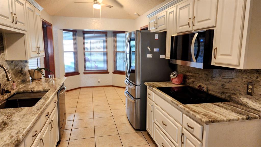 7505 Patsy Court Arlington, TX 76016 - Photo 14 of 38 Kitchen featuring black appliances, light tile patterned floors, a textured ceiling, a textured wall, dolomite countertops, and white cabinetry.