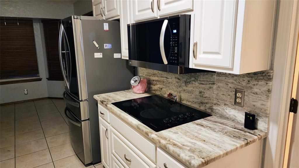 7505 Patsy Court Arlington, TX 76016 - Photo 16 of 38 Kitchen featuring black appliances, light tile patterned floors, a textured ceiling, a textured wall, dolomite countertops, and white cabinetry.