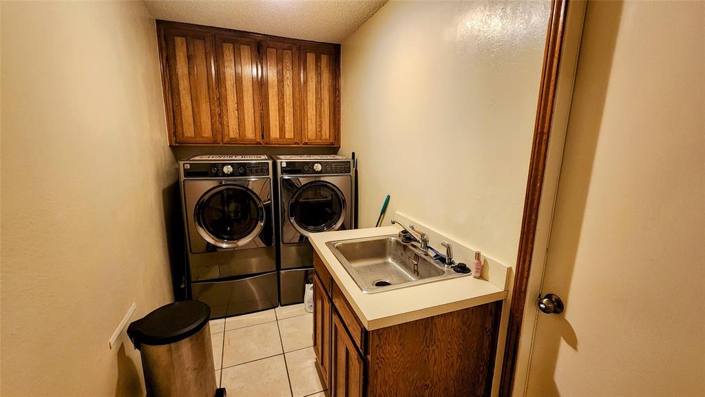 7505 Patsy Court Arlington, TX 76016 - Photo 30 of 38 Washroom featuring wood cabinet space, a textured ceiling, light tile patterned flooring, washer and clothes dryer.