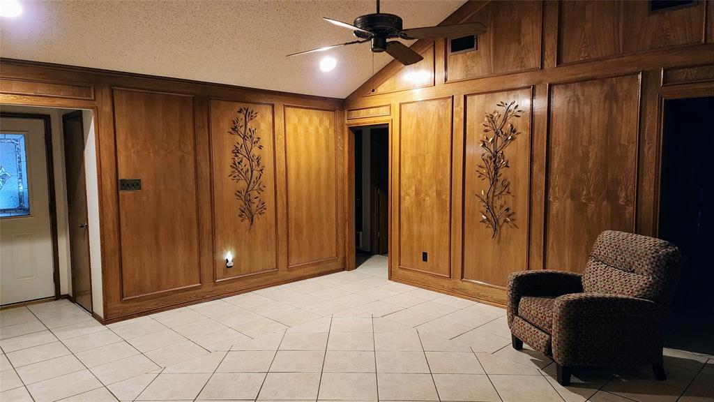 7505 Patsy Court Arlington, TX 76016 - Photo 6 of 38 Living room with lofted ceiling, light tile patterned floors, a ceiling fan, and picture frame paneling walls.