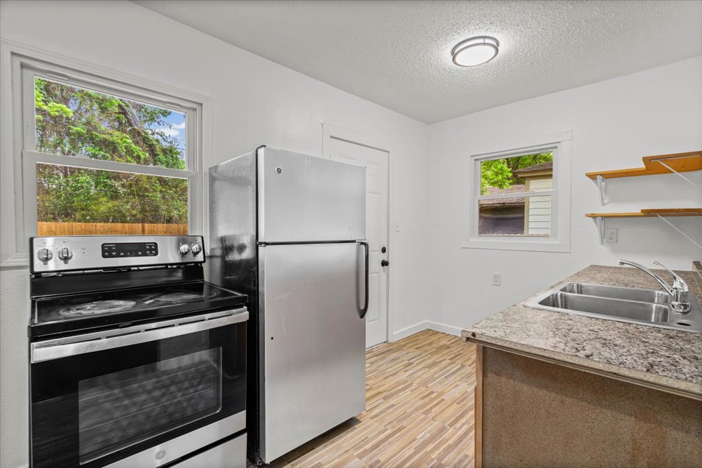 2206 Rountree Drive Austin, TX 78722 - Photo 5 of 16 Kitchen featuring stainless steel appliances, light wood-style flooring, a textured ceiling, light countertops, and open shelves