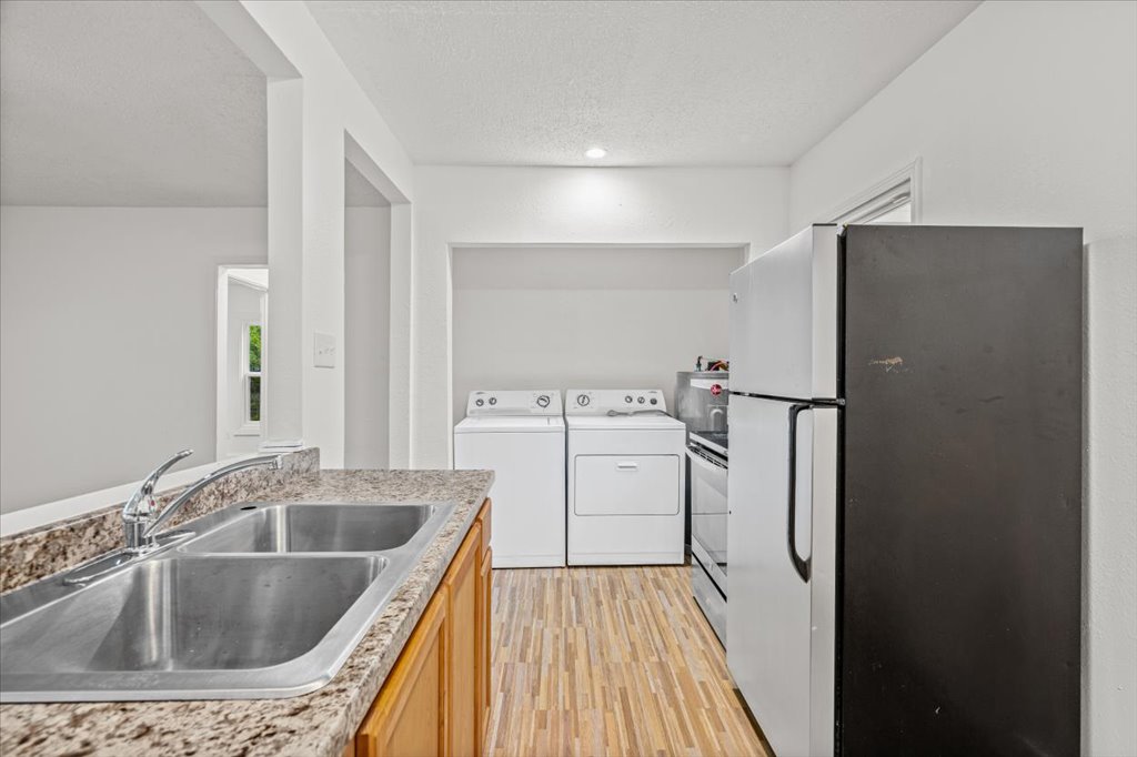 2206 Rountree Drive Austin, TX 78722 - Photo 7 of 16 Kitchen featuring stainless steel appliances, light countertops, separate washer and dryer, light wood-style flooring, and a textured ceiling
