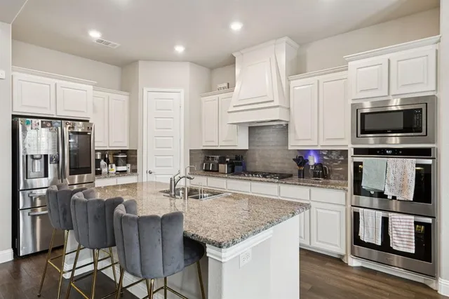 a kitchen with stainless steel appliances granite countertop a stove top oven a refrigerator a sink and white cabinets