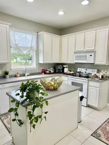 a kitchen with stainless steel appliances granite countertop a sink a stove a refrigerator white cabinets and a window