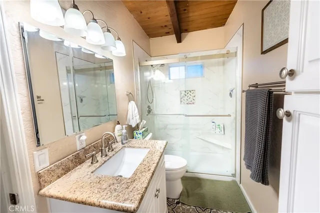 a bathroom with a granite countertop sink a toilet a mirror and shower