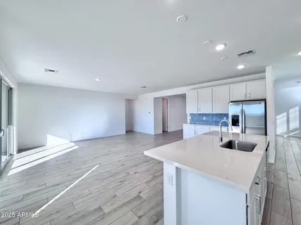 a kitchen with stainless steel appliances a sink dishwasher a refrigerator and white cabinets with wooden floor