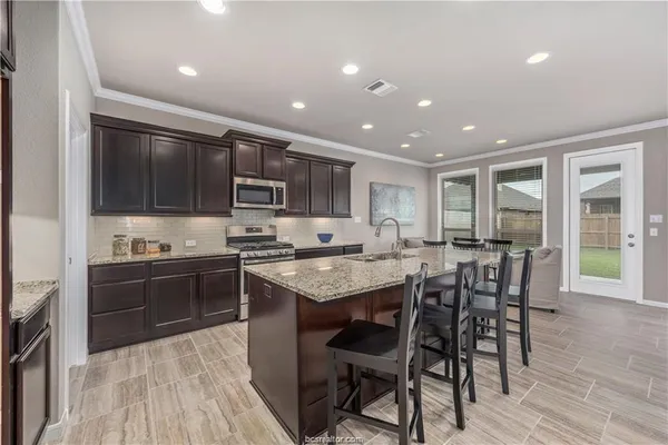 a kitchen with stainless steel appliances granite countertop a stove top oven a sink dishwasher a dining table and chairs with wooden floor
