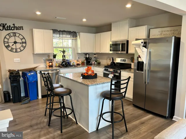 a kitchen with stainless steel appliances granite countertop a refrigerator a stove top oven a sink dishwasher and a dining table with wooden floor