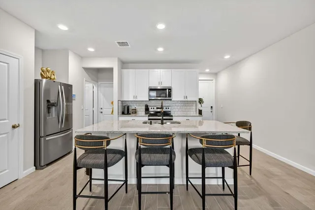 a kitchen with stainless steel appliances granite countertop a dining table chairs refrigerator and microwave