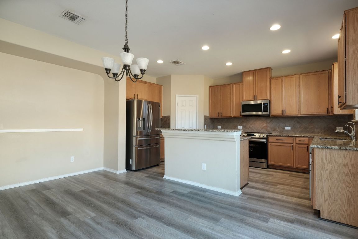 1244 Yellow Iris Road Leander, TX 78641 - Photo 8 of 25 a kitchen with granite countertop a refrigerator oven a sink dishwasher and white cabinets with wooden floor