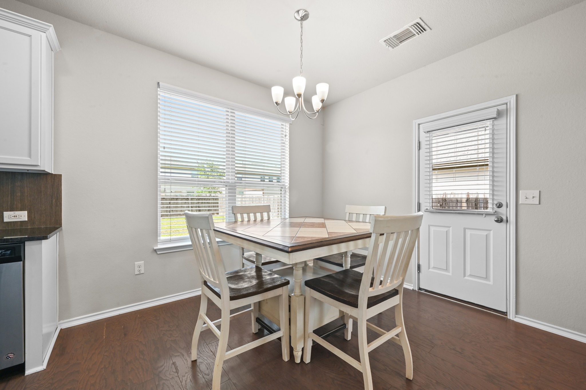 209 Noddy Road Buda, TX 78610 - Photo 9 of 30 Dining area featuring wood-finish flooring, a contemporary chandelier, a window with blinds, and a white door with integrated blinds