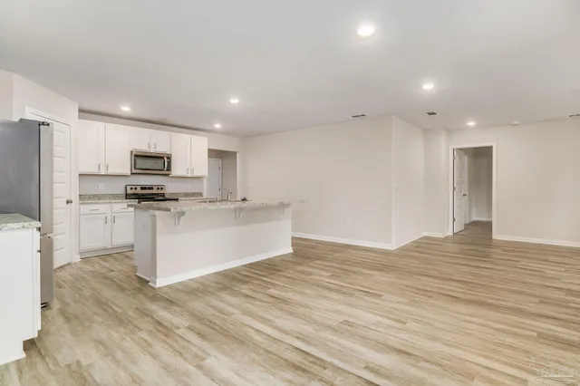 a large kitchen with kitchen island a stove a sink dishwasher a refrigerator and white cabinets with wooden floor